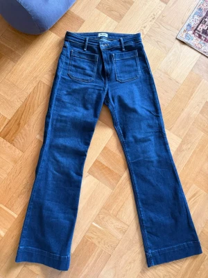 Mörkblå utsvängda jeans med fickor - Säljer ett par mörkblå jeans med utsvängda ben och stora fickor fram. Jeansen har hög midja och klassiska bakfickor. Snygg retrostil som passar perfekt till sneakers eller boots. Materialet är denim med lite stretch för extra komfort. w29 L30.