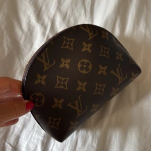Brun trendig modern och helt ny monogram necessär el sminkväska  - Säljer en klassisk brun necessär el sminkväska i praktisk modell med snyggt monogrammönstrer. Halvmåneformad modell med dragkedja upptill. Perfekt för smink eller småprylar.