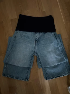 Unika lager-på-lager jeanssbyxor - Säljer ett par riktigt coola jeanbyxor med lager-på-lager-effekt. Shortsen har en hög midja med svart stretchpanel upptill och är sydda i ljusblå denim. Perfekt för dig som vill sticka ut med en kreativ och edgy stil.