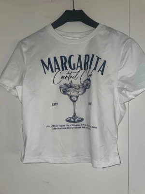 Tre  vita t-shirts med cocktailtryck - Säljer tre vita t-shirts med coola cocktailmotiv och tryck framtill.  Alla tre har korta ärmar och är i mjuk bomull. Perfekta för en avslappnad och trendig look. Dem är korta i längden lite mer crop 