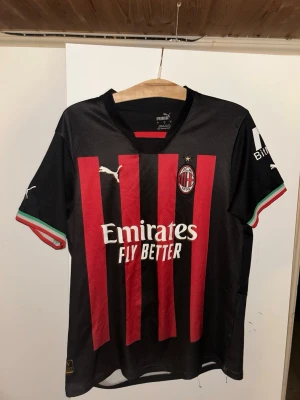 AC Milan matchtröja Ibrahimović 11 - Snygg AC Milan matchtröja från Puma med Ibrahimović och nummer 11 på ryggen. Tröjan är svart med röda ränder, vita logotyper och italienska flaggdetaljer på ärmsluten. Tillverkad i lätt och ventilerande material, perfekt för fotboll eller träning.