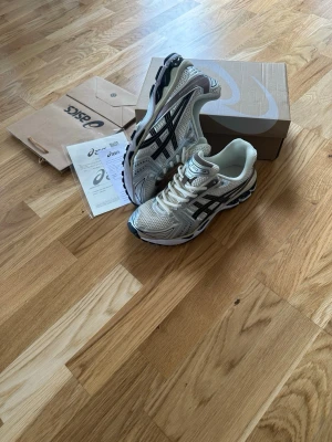 Asics gel kayano 14 - Snygga sneakers från Asics i vitt meshmaterial med silver- och svarta detaljer. Skorna har en sportig design med tydliga Asics-loggor på sidorna och en rejäl sula för bra komfort. Perfekta för dig som gillar streetwear och sportig stil.