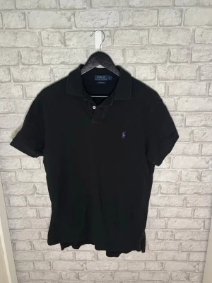 Ralph Lauren piké  - Ralph Lauren piké i svart med lila broderad logga och Custom Fit-passform. Klassisk modell i skön bomull och väldigt fint skick. Hör gärna av dig vid intresse! 🙌