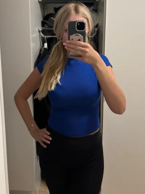 Blå croppad topp med öppen rygg - Snygg blå croppad topp med korta ärmar och öppen rygg. Perfekt för dig som vill ha en enkel men ändå trendig topp till din outfit. T-shirten har en tight passform och är tillverkad i ett mjukt stretchigt material.