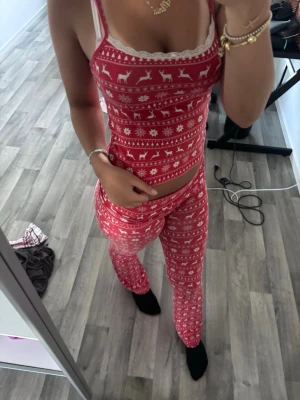 Röd/vita pyjamas med jul tema - Supermysig röd pyjamas med vitt julmönster av renar och snöflingor. Setet består av ett linne med spetskant och matchande yoga pants settey är från Gina Tricot använt 1 gång och inte mer dom är som nya 