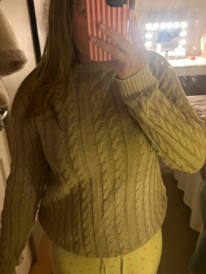 Beige kabelstickad tröja - Säljer en beige kabelstickad tröja med rund hals och ribbade muddar. Tröjan har ett klassiskt flätmönster och är perfekt för att hålla sig varm under kyliga dagar. Passar till många olika stilar och är superenkel att matcha med andra plagg.