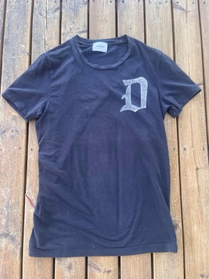 Svart t-shirt från Dondup med tryck - Snygg svart t-shirt från Dondup med ett stort D-tryck i vitt på bröstet. Klassisk rund halsringning och korta ärmar. Tillverkad i mjuk bomull som känns skön mot huden. Perfekt för dig som gillar stilrena plagg med en twist.