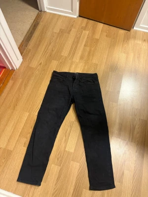 Svarta tapered / Mike  jeans - Säljer ett par svarta tapered jeans med klassisk femficksdesign och normal midja. Jeansen har en smalare passform nedtill och är perfekta för dig som gillar en clean och enkel stil. Materialet känns mjukt och stretchigt för extra komfort.