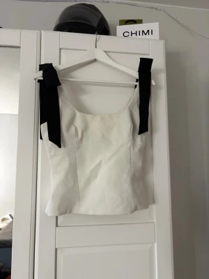 Vit linnetopp med svarta band Zara - Snygg vit linnetopp från Zara med breda svarta knytband på axlarna. Toppen har en rak passform och är tillverkad i ett slätt material som ger en stilren look. Perfekt att styla med jeans eller kjol för en trendig outfit.