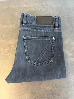 Z Zegna Mörkblå raka jeans, stl 31 - Snygga mörkblå jeans med raka ben och klassisk femficksdesign. Jeansen har en diskret tvättad look och silverfärgade nitar. Passar perfekt till en avslappnad stil och har bälteshällor i midjan. Materialet är mjukt denim för skön känsla.