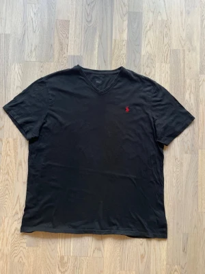 Polo Ralph Lauren v-neck T-shirt - svart, XL - Bra skick. Inga tydliga tecken på användning T-shirt från Polo Ralph Lauren, storlek XL, svart V-ringning, röd logga vänster bröst Bröstvidd: 59 cm Längd: 74 cm Inga defekter, normalt slitage