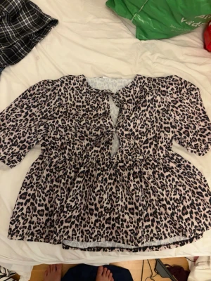 Leopardmönstrad blus från Stories - Säljer en snygg leopardmönstrad blus från Stories i storlek M (40-42). Blusen har trekvartsärm, v-ringning med knytning framtill och en luftig passform. Perfekt för dig som gillar djurmönster och vill sticka ut lite extra.