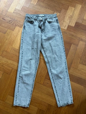 Grå jeans från Gina Tricot - Säljer ett par grå jeans från Gina Tricot i storlek 36. Jeansen har hög midja, raka ben och klassisk femficksmodell. Materialet är denim i tvättad grå färg med dragkedja och knapp framtill. Perfekta till en avslappnad och trendig look.