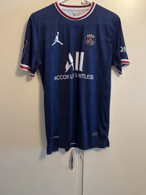 PSG matchtröja Messi #30 blå - Säljer en blå PSG matchtröja med Messi och nummer 30 på ryggen. Tröjan har vita och röda detaljer vid krage och ärmslut, samt klubbmärke och sponsortryck på bröstet. Tillverkad i lätt och ventilerande material, perfekt för fotbollsträning eller support.