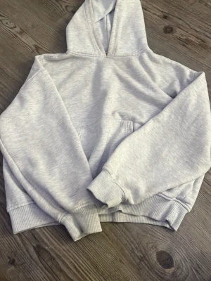 Ljusgrå hoodie med huva - En stilren ljusgrå hoodie med klassisk huva och magficka. Hoodien har ribbade muddar vid ärmslut och nederkant. Perfekt för en avslappnad och trendig look. Tillverkad i mjukt sweatshirtmaterial som känns skönt mot huden.