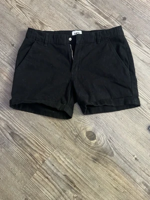 Svarta shorts med dragkedja - Klassiska svarta shorts med normal passform och dragkedja framtill. Shortsen har bälteshällor och två fickor på sidorna. Perfekta till sommaren och enkla att matcha med olika stilar.