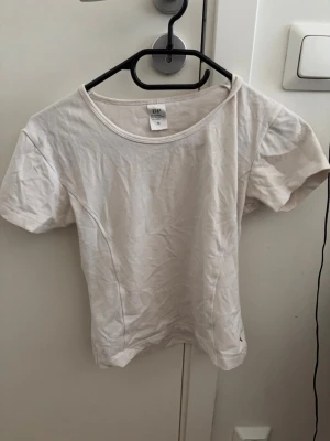 Vit basic t-shirt med rund hals - En enkel vit t-shirt med rund halsringning och korta ärmar. Tillverkad i mjuk bomull, perfekt för en clean och avslappnad stil. Passformen är normal och tyget är lätt och bekvämt.