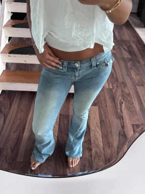 Low waist True religion jeans - Säljer ett par ljusblå bootcut jeans med låg midja och klassisk femficksmodell. Jeansen har en snygg tvätt med slitningar framtill och är tillverkade i ett mjukt denimtyg som sitter skönt på kroppen. Perfekta för en avslappnad och trendig look. Jag säljer dom för dom är för stora på mig jag har använt dom 2-3 gånger och det finns ett håll längst ner på dom eftersom dom vart för långa för mig men är knappt använda💕