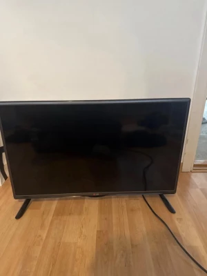 Svart platt-TV från LG - Säljer en svart platt-TV från LG med stilren design och två ben. TV:n har flera anslutningar på baksidan, inklusive HDMI, SCART och komponentingångar. Perfekt för filmkvällar eller gaming. Strömkabel medföljer.