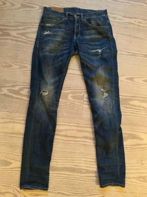 Dondup George  - Säljer ett par blå dondup jeans med slitningar och distressed detaljer på både fram- och baksida. Jeansen har klassisk femficksmodell och kontrastsömmar. Perfekta för en avslappnad och trendig look.