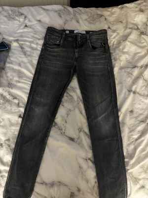 Replay Bronny svarta slim jeans strl 28  - Säljer ett par svarta Replay Bronny jeans med slim fit och snygga slitningar. Jeansen har klassisk femficksdesign, dragkedjegylf och är tillverkade i stretchigt denim för extra komfort. Perfekta för dig som gillar en modern och stilren look.