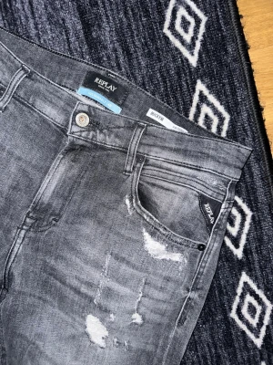 Grå slitna jeans från Replay - Säljer ett par grå jeans från Replay med slitningar och distressed detaljer. Jeansen har smal passform, klassisk femficksmodell och knappgylf. Perfekta för en avslappnad och trendig look. Tags samt ordinarie påse och kvitto finns! 