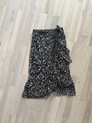 Leopardmönstrad omlottkjol Gina Tricot - Säljer en snygg leopardmönstrad omlottkjol från Gina Tricot. Kjolen har volangdetaljer och knyt i sidan, vilket ger en trendig look. Tillverkad i mjuk polyester med lite stretch för extra komfort.