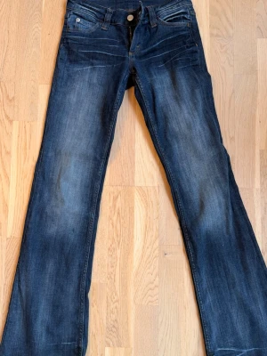 Mörkblå weekday bootcut jeans  - Säljer ett par mörkblå bootcut jeans med snygga slitningar och tvättade detaljer. Klassisk femficksmodell med knapp och dragkedja framtill. Jeansen har en lätt utsvängd passform nedtill och är perfekta för en avslappnad och trendig look.