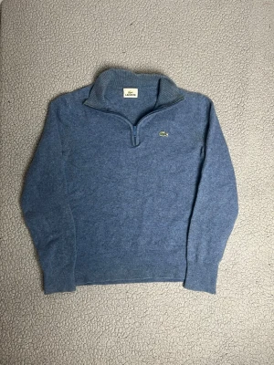 Blå stickad tröja från Lacoste - Snygg blå stickad tröja från Lacoste med halv dragkedja. Mycket bra skick. Sitter som xs/s