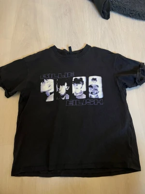 Svart Billie Eilish t-shirt - Cool svart t-shirt med tryck av Billie Eilish och fyra olika porträtt på framsidan. T-shirten har rund hals och korta ärmar. Materialet ser ut att vara mjuk bomull, perfekt för dig som gillar musik och streetwear.
