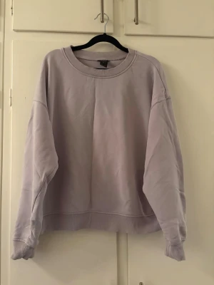 Ljuslila oversized sweatshirt - En stilren ljuslila sweatshirt i oversized modell med rund halsringning och breda muddar vid ärmslut och nederkant. Tröjan är tillverkad i mjukt bomullsmaterial och har en enkel, minimalistisk design utan tryck eller detaljer.