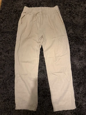 Beiga linnebyxor - Snygga beiga linnebyxor med avslappnad passform. Byxorna har sidofickor dock har en av de ett stort hål i sig! Perfekta för en chill och stilren look. Tillverkade i lätt och luftigt linnematerial. Lite slitna längst ner! 