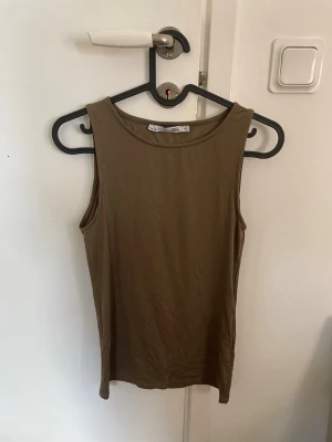 Brun ärmlös linnetopp - Säljer en enkel och stilren brun linnetopp med rund halsringning. Toppen är ärmlös och har en rak passform, perfekt att matcha med jeans eller kjol. Materialet känns mjukt och lätt mot huden.