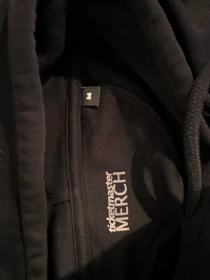Svart hoodie med tryck från Ticketmaster - Svart hoodie med vit text 'Helt Seriöst?!' på framsidan. Klassisk huva med snören och ribbade muddar. Perfekt för dig som gillar merch och vill ha en chill look. Materialet är mjukt och bekvämt, passar till många olika outfits. Jag fick den av Khalifa 