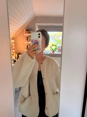 Beige oversized teddyjacka - Säljer en supermjuk och oversized teddyjacka i beige med stora fickor framtill och tryckknappar. Jackan har rund halsringning och är perfekt för dig som vill ha en mysig och trendig look. Passar till lager på lager och är riktigt skön under kyliga dagar. 