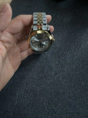 Silver och guld armbandsur - Stilren klocka med armband i silver och guldton. Urtavlan är ljus med markerade index och guldfärgade visare. Boetten har en räfflad guldkant som ger en exklusiv känsla. Perfekt accessoar för dig som gillar klassisk och tidlös design.