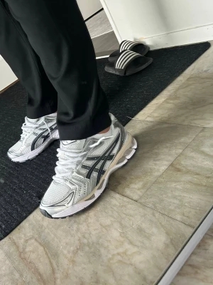 Silverfärgade Asics sneakers - Snygga sneakers från Asics i silver och vitt med svarta detaljer. Skorna har en sportig design med mesh- och syntetmaterial, samt en rejäl sula för extra komfort. Perfekta för dig som gillar en clean och modern stil.