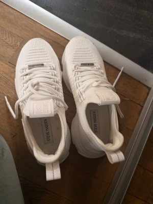Vita Steve Madden sneakers - Snygga helvita sneakers från Steve Madden med chunky sula och stickad ovandel i mesh. Skorna har vita snören, diskreta detaljer och en modern, sportig look. Perfekta för dig som gillar stilrena och trendiga sneakers.