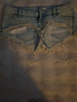 Ljusblå jeansshorts med fransar - Snygga ljusblå jeansshorts med slitna detaljer och fransig kant. Klassisk femficksmodell med knapp och dragkedja framtill. Perfekta för varma dagar och en avslappnad stil.