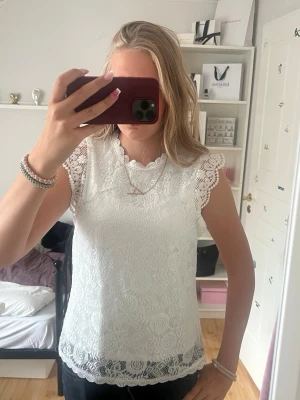 Vit spetsblus med kort ärm - Säljer en söt vit blus i spets med fina detaljer och korta ärmar. Blusen har rund halsringning och vackert mönstrad spets längs kanterna. Perfekt att styla med både jeans och kjol för en trendig look.