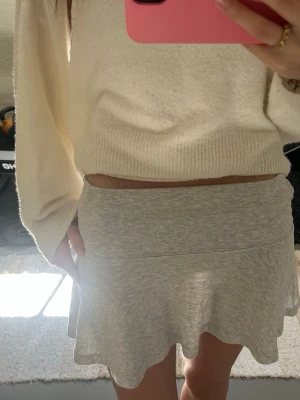 Grå kortkjol med volangkant - Supersöt grå kortkjol med bred midjeresår och volangkant nertill. Kjolen har en mjuk och bekväm känsla, perfekt för en avslappnad och trendig look. Passar till både stickade tröjor och crop tops.