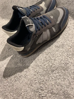 Valentino Garavani sneakers blå/grå - Snygga sneakers från Valentino Garavani i blått och grått med mesh och mockadetaljer. Skorna har mörkblå snören, vit häl och coolt mönster på sidan. Perfekta för dig som gillar streetstyle och exklusiva märken.