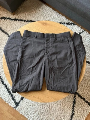 Mörkgrå kostymbyxor - Hej! 👋 Säljer dessa snygga mörkgrå kostymbyxor från H&M i slim fit-modell🤩 Byxorna har klassisk design med bälteshällor och raka ben😮‍💨 Materialet är en mix av polyester, viskos och elastan för skön stretch och passform😌Perfekta för en stilren look🧼 Meddela vid frågor📩
