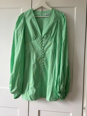 Grön kortklänning från Adoore - Snygg ljusgrön kortklänning från Adoore med långa puffärmar och små blommiga detaljer. Klänningen har v-ringning, knappar framtill och är tillverkad i ett lätt bomullstyg. Perfekt för vår och sommar!