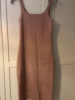 Beige ärmlös klänning med slits - Säljer en enkel och stilren beige klänning i stretchigt material. Klänningen är ärmlös med breda axelband och har en liten slits nedtill på baksidan för extra rörelsefrihet. Perfekt för dig som gillar minimalistisk design.