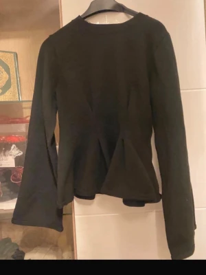 Svart långärmad topp med utsvängd midja - Snygg svart långärmad topp med rund halsringning och utsvängd midja som ger en feminin siluett. Perfekt att styla med jeans eller kjol för en trendig look.