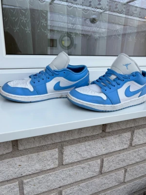 Blåvita sneakers med klassisk design - Snygga sneakers i blått och vitt med lågt skaft och klassisk siluett. Skorna har vit bas med blå detaljer och matchande blå snörning. Ovandelen är i läder och tungan är ljusgrå med en blå logga. Perfekta för dig som gillar streetwear och sportig stil.