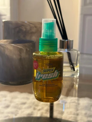 Super Fresh parfym body mist - Super Fresh parfym body mist i en genomskinlig plastflaska med grön spraypump och gul vätska. Flaskan rymmer 100 ml och har en modern, sportig design med färgglad etikett. Perfekt för dig som vill ha en fräsch och lätt doft. Helt oanvänd