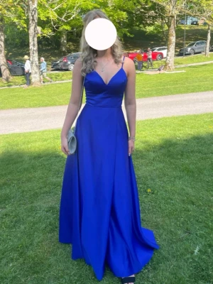 Kornblå balklänning med snörning - Elegant kornblå långklänning med smala axelband, v-ringning och snygg snörning i ryggen. Klänningen har en figurnära överdel och ett svepande kjolparti i ett glansigt material som ger en lyxig känsla. Perfekt för bal eller student. Använd 1 gång, älskade den. 