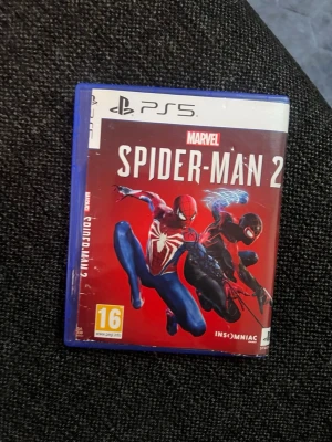 Marvel Spider-Man 2 PS5 spel - Marvel Spider-Man 2 till PS5 med snyggt röd omslag där både Spider-Man och Miles Morales syns i action. Spelet är från Insomniac Games och har PEGI 16-märkning. Perfekt för dig som gillar superhjälteäventyr och snabba actionspel.